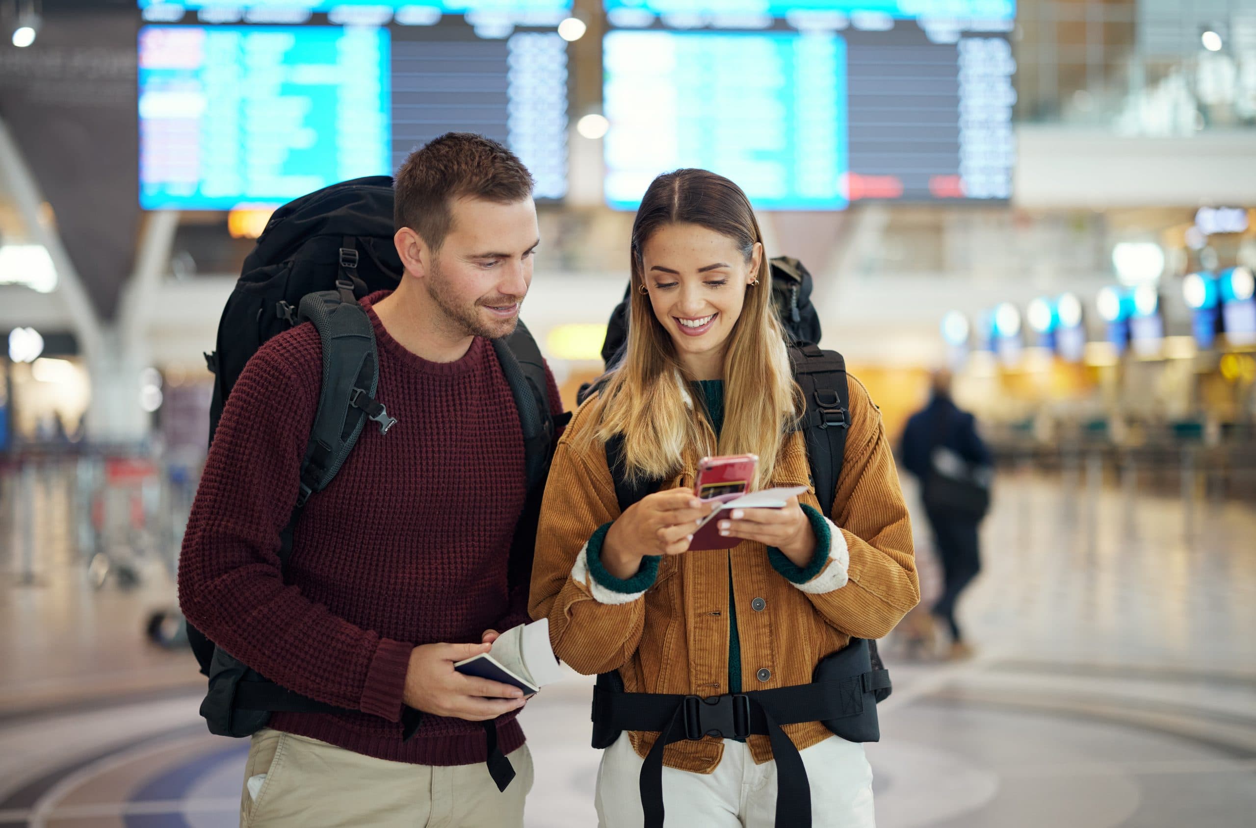 Een stel met rugzakken bekijkt een telefoon en reisdocumenten op de luchthaven.
